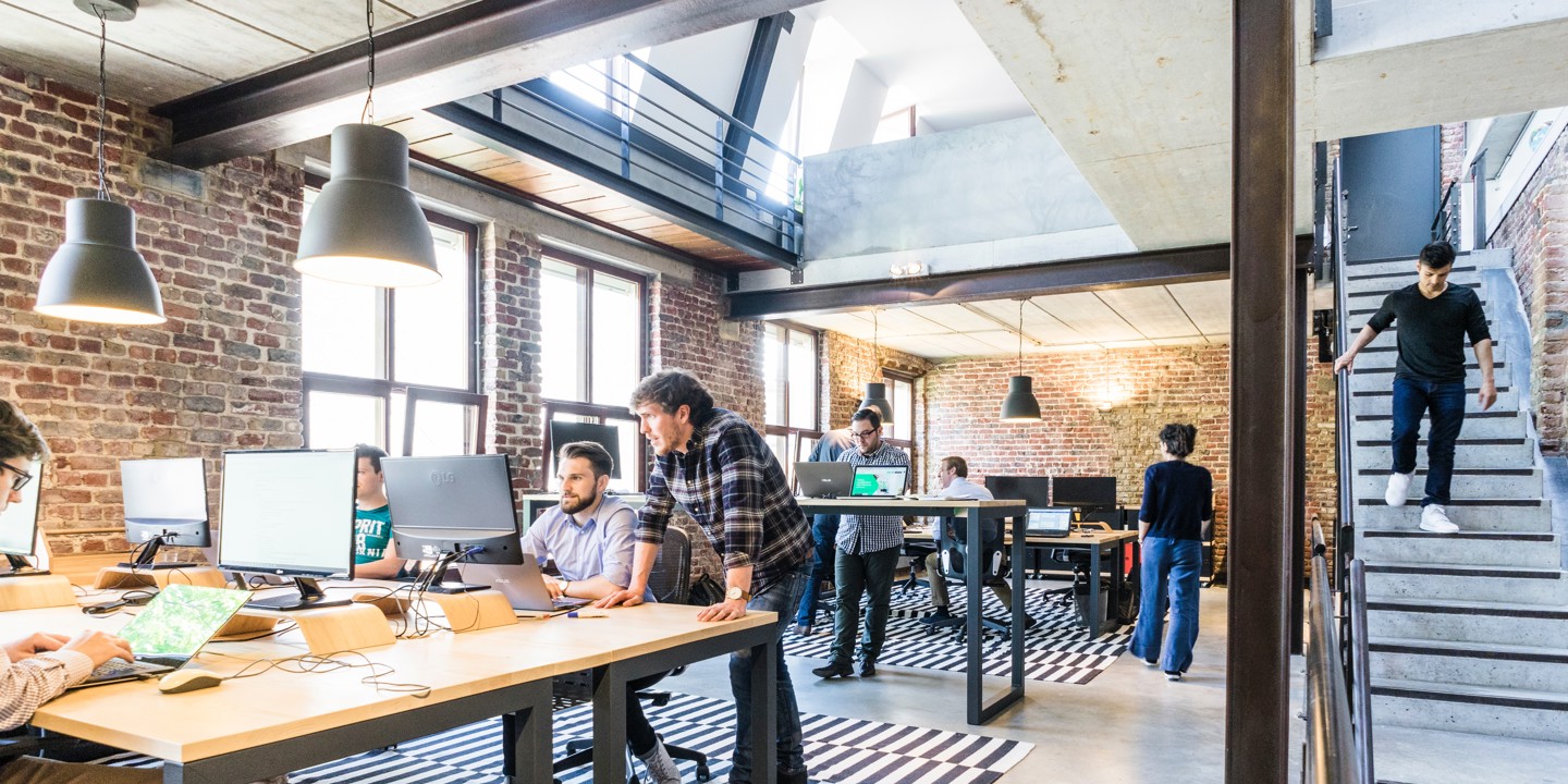Open plan office with long tables and laptops with brick interior and wooden floor and stairs