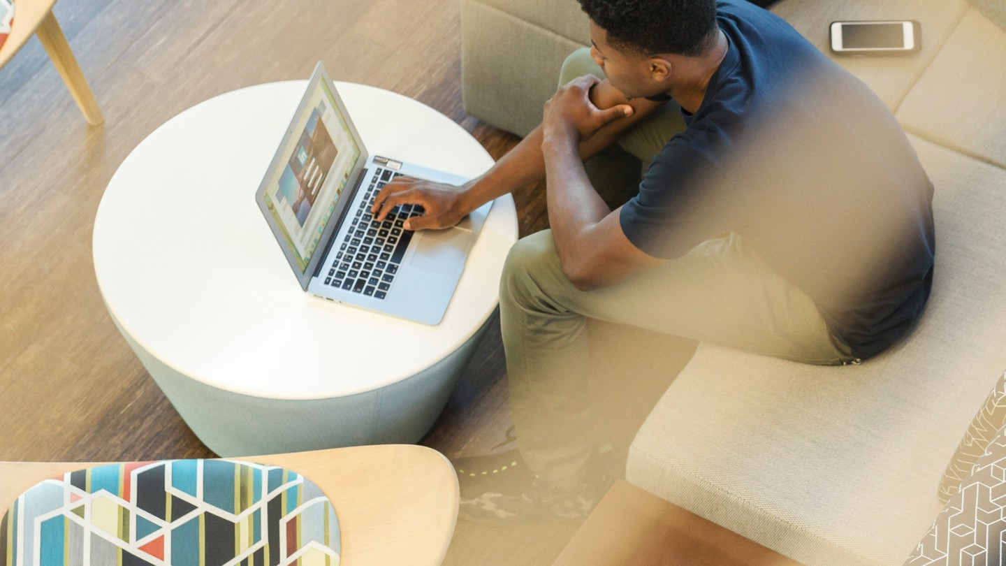 A shot through a 2nd floor interior window of a man on his laptop